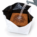 Watering can hydrating the compressed coco brick inside the open 30L Coco Grow Pot
